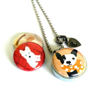 May include: A silver chain necklace with a heart charm and two round pendants. One pendant features a black and white dog wearing a yellow and white polka dot scarf. The other pendant features a white dog on a red background.