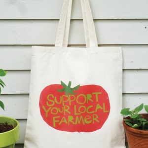 May include: A white canvas tote bag with a red tomato graphic and the text "Support Your Local Farmer" in green letters.