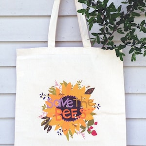 May include: A white canvas tote bag with a sunflower design and the text "Save the Bees".