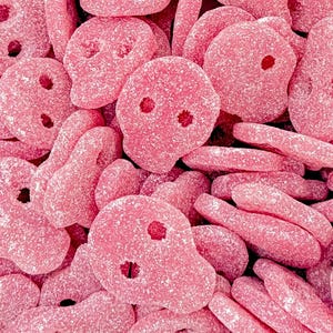 May include: A close-up shot of a pile of pink gummy sweets. The sweets are shaped like skulls and other forms. They are coated in sugar, giving them a slightly rough texture. The sweets are a vibrant pink colour.