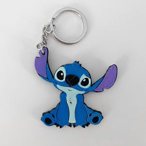 Pode incluir: Um chaveiro de pl&aacute;stico com o personagem Stitch, azul e roxo. O chaveiro tem um anel de metal prateado.