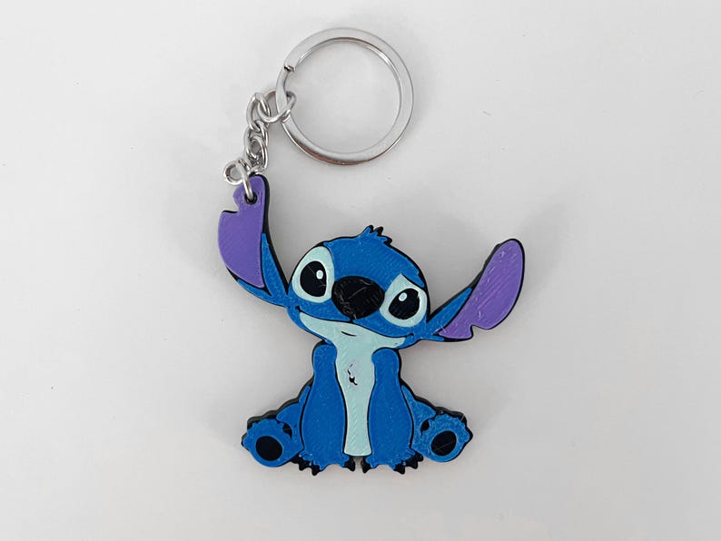 Pode incluir: Um chaveiro de pl&aacute;stico com o personagem Stitch, azul e roxo. O chaveiro tem um anel de metal prateado.