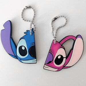 Pode incluir: Dois chaveiros de Stitch azul e rosa com correntes prateadas. O Stitch azul est&aacute; &agrave; esquerda e o Stitch rosa &agrave; direita.