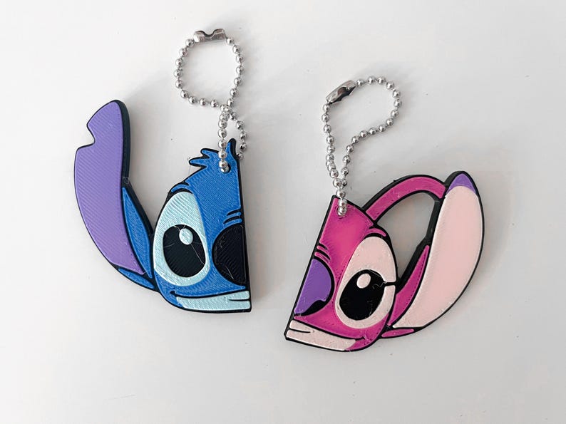 Pode incluir: Dois chaveiros de Stitch azul e rosa com correntes prateadas. O Stitch azul est&aacute; &agrave; esquerda e o Stitch rosa &agrave; direita.