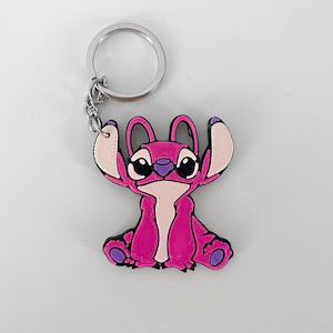Pode incluir: Chaveiro Stitch rosa com um chaveiro prateado. O chaveiro apresenta um personagem de desenho animado Stitch com olhos grandes e um corpo rosa.