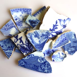 May include: A collection of broken porcelain shards with blue and white floral patterns. The fragments vary in size and shape, displaying intricate designs and a distressed aesthetic. The pieces are scattered, revealing the edges of the broken pottery.