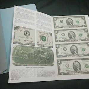 May include: A light blue envelope with a printed sheet featuring images of United States two-dollar bills. The sheet also includes text and images of the Declaration of Independence. The bills feature a portrait of Thomas Jefferson.