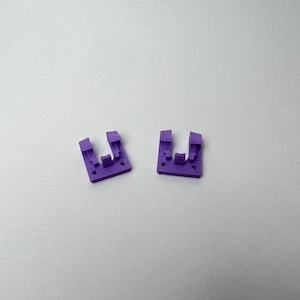 Può includere: Due clip di plastica viola con un'apertura a forma di U. Le clip sono progettate per tenere insieme gli oggetti.