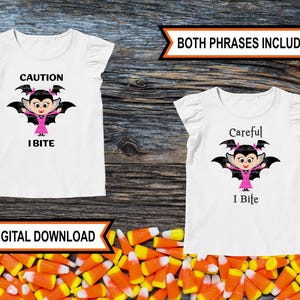 May include: Two white t-shirts with a cartoon vampire girl graphic. One shirt says "Caution I Bite" and the other says "Careful I Bite".
