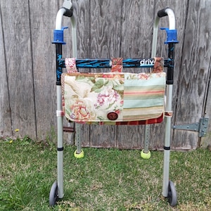 May include: A silver walker with a colorful patchwork fabric bag attached. The bag features floral, striped, and patterned fabrics. The walker has blue accents and the word "driv" printed on the frame.