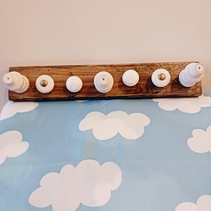 May include: A wooden coat rack with seven white ceramic knobs. The knobs are attached to a rectangular, dark brown wooden board. Some knobs have gold accents. The rack is mounted above a blue surface with white cloud shapes.