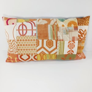 May include: Rectangular patchwork pillow featuring a variety of orange, cream, and green fabric patterns. The pillow's design includes geometric shapes, floral motifs, and textured fabrics, creating a unique and colorful decorative item.