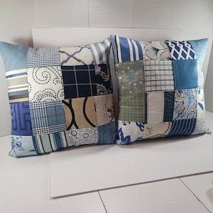 May include: Two square throw pillows with patchwork designs in various shades of blue, white, and beige. The pillows feature a mix of patterns, including stripes, floral prints, and geometric shapes, creating a cozy, decorative accent.