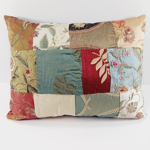 May include: Rectangular patchwork pillow with a variety of fabrics in shades of gold, green, red, and blue. The pillow features floral and leaf patterns, with embroidered details. The pillow is a decorative home accent.