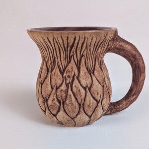 May include: A brown ceramic mug with a textured design resembling a pinecone. The mug has a rounded body and a handle.