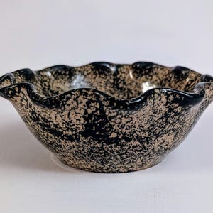 May include: A black and cream ceramic bowl with a scalloped rim. The bowl has a speckled glaze.