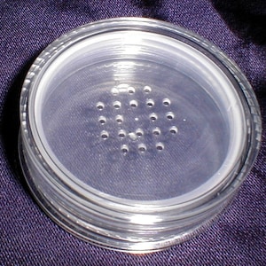 May include: A clear plastic container with a round, perforated lid. The lid has a series of small holes for dispensing powder.