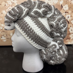 May include: A white and gray crocheted hat with a unique, textured design. The hat is made with a combination of white and gray yarn and has a fluffy, voluminous look.