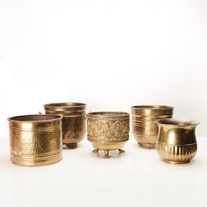 May include: Five brass planter pots of varying sizes and designs. The pots are all made of a shiny, gold-coloured metal. Some of the pots have decorative patterns, while others are plain.