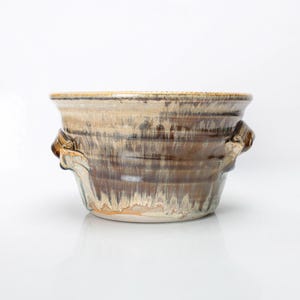 Peut inclure: Un bol en céramique brun et blanc avec deux anses. Le bol a un glaçage marbré et un aspect rustique.