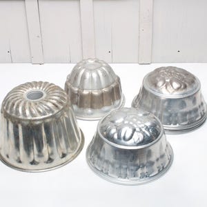 Op de afbeelding: Vier zilveren metalen gelei-vormen, twee met een geribbeld ontwerp en twee met een bloemenpatroon.