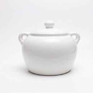 Peut inclure: Un sucrier en céramique blanche avec un corps arrondi, deux petites anses latérales et un couvercle assorti doté d'un bouton central. L'objet présente une finition lisse et brillante ainsi qu'une base large qui se rétrécit vers le haut.