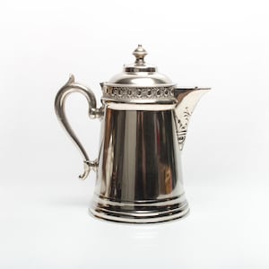 Peut inclure: Une carafe en argent avec un motif orné autour du haut et une poignée décorative.