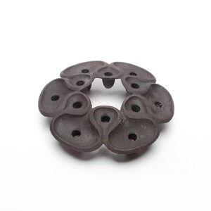 May include: A dark brown, circular decorative object with a series of interconnected, organic-shaped elements. Each element has a small, circular hole. The object is set against a white background, highlighting its unique form and texture.