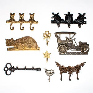 May include: A set of decorative key hooks featuring a variety of designs, including cats, turtles, a car, a bird, and roses. The hooks are made of metal and have a vintage style.
