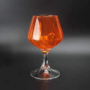 Peut inclure: Un gobelet en verre transparent avec un large bol et une longue tige. Le bol est orange.