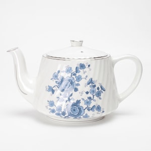 Peut inclure: Théière en céramique blanche avec couvercle et anse. La théière présente un motif floral bleu et une bordure argentée. Le bec et la poignée sont incurvés. Conçu pour infuser le thé.