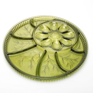 Peut inclure: Un plat de service vintage en verre vert avec une section centrale en forme de fleur et plusieurs compartiments en forme de feuilles. Le plat a un bord texturé et est conçu pour servir des apéritifs ou des collations. Le design est élégant et fonctionnel.
