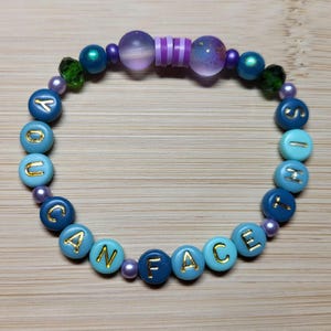 K&ouml;nnte beinhalten: Ein Perlenarmband mit den Worten "YOU CAN FACE IT" in goldenen Buchstaben auf blauen und t&uuml;rkisfarbenen Perlen. Das Armband hat auch lila, gr&uuml;ne und irisierende Perlen.