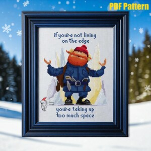 Op de afbeelding: Borduurpatroon met een cartoonfiguur met een rode muts en baard, die op een besneeuwde berg staat. De tekst luidt "Als je niet op de rand leeft, neem je te veel ruimte in beslag".