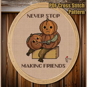 Puede incluir: Un patrón de punto de cruz con dos figuras con cabeza de calabaza y el texto "NEVER STOP MAKING FRIENDS". El diseño está dentro de un marco ovalado, sobre un fondo de madera. Las palabras "PDF Cross Stitch Pattern" están en la parte superior.