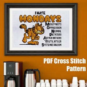 May include: A framed cross-stitch featuring Garfield with the words "I Hate Mondays." Additional text lists "Misogynists, Oppression, Normal Dictators, Aryan Nations, Youth, Hitler, Systemic Racism." The image is framed in black.