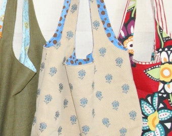 May include: Three different fabric tote bags. The first bag is a solid olive green. The second bag is a cream color with a blue floral pattern. The third bag is red with a black, white, and yellow floral pattern.