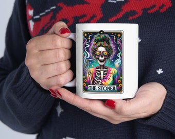 May include: White ceramic mug with a colorful illustration of a skeleton wearing tie-dye and sunglasses, smoking a joint. The text "THE STONER" is printed below the image.