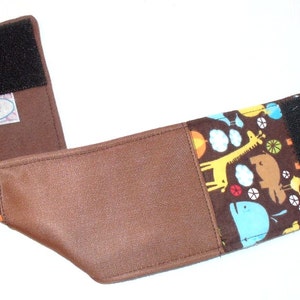 May include: A brown baby carrier strap with a colorful animal print and a black Velcro closure. The strap features a brown faux leather center and a tag that reads "spot Noiz".