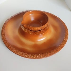 May include: A two-tone brown ceramic chip and dip serving dish. The outer rim has a decorative scroll design. The centre bowl is raised and has a small spout. The dish is ideal for serving snacks at parties.