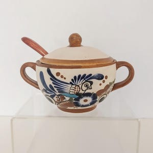 Peut inclure: Un sucrier en céramique avec un couvercle et deux anses, orné d'un motif peint à la main d'oiseaux et de fleurs bleues, marron et crème. Une cuillère en bois est à l'intérieur. Le bol mesure environ 10 cm de diamètre.