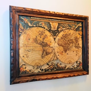 May include: A framed antique-style world map print featuring two circular hemispheres with detailed cartography, surrounded by decorative illustrations of figures and animals, enclosed in a dark brown, textured, scalloped wooden frame.