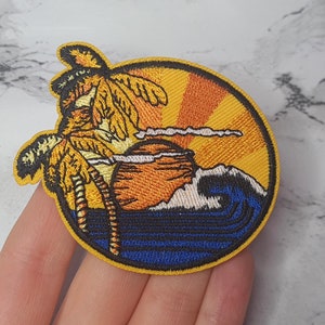 May include: Embroidered iron-on patch featuring a sunset scene with palm trees, a wave, and a sun. The patch is yellow, orange, blue, and white.