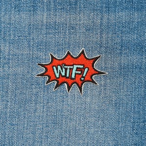 May include: A red and black embroidered patch with the text "WTF!" in a blue font. The patch is in the shape of a comic book speech bubble.
