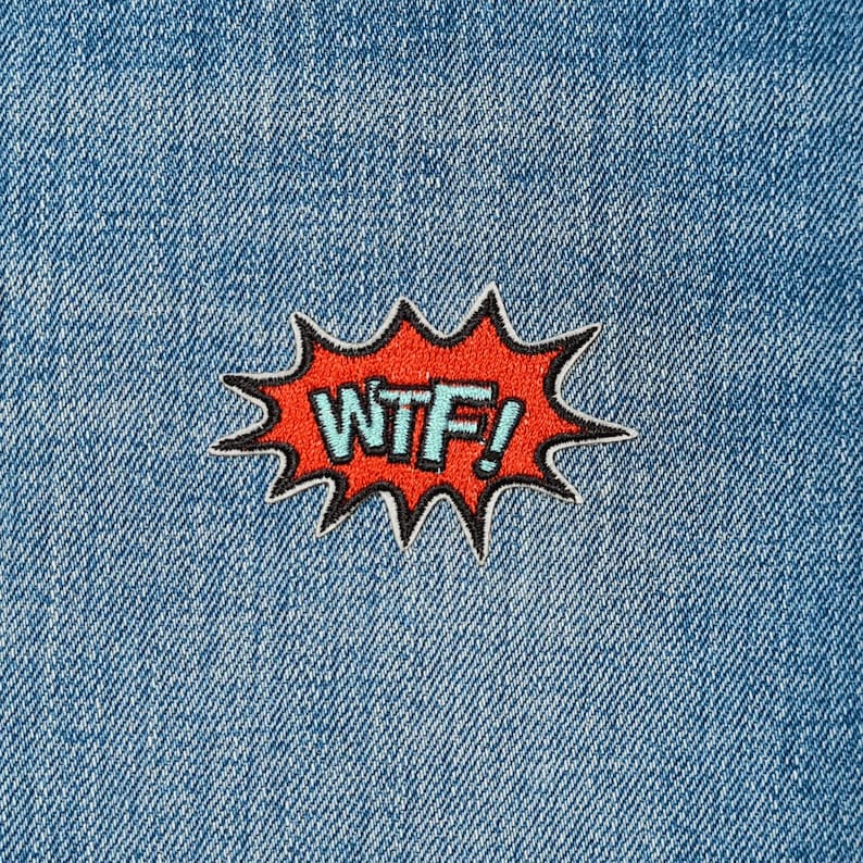 May include: A red and black embroidered patch with the text "WTF!" in a blue font. The patch is in the shape of a comic book speech bubble.