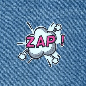 May include: A blue denim fabric with a pink and white embroidered patch that says "ZAP!" in a comic book style font.