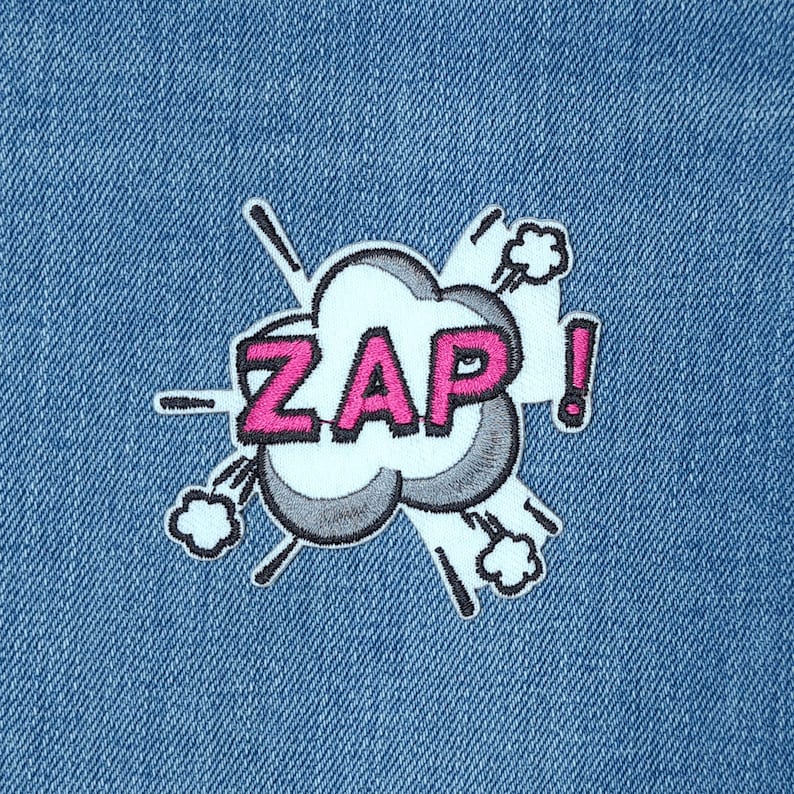 May include: A blue denim fabric with a pink and white embroidered patch that says "ZAP!" in a comic book style font.
