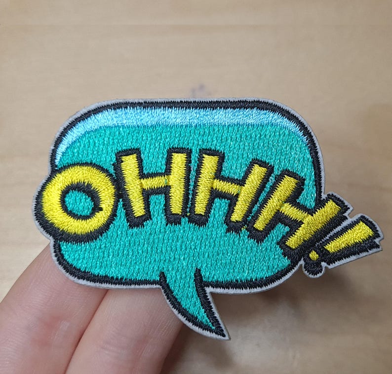 May include: A turquoise blue speech bubble with a yellow embroidered "OHHH!" inside. The speech bubble has a black outline and a white border.