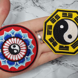 May include: Two embroidered patches featuring the yin yang symbol. One patch is red with a blue and white flower design, the other is yellow with a black and white yin yang symbol surrounded by black and yellow lines.