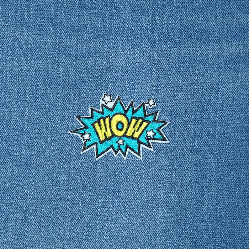 May include: A blue and yellow embroidered patch with the word "WOW" in a comic book style font. The patch is surrounded by white stars.